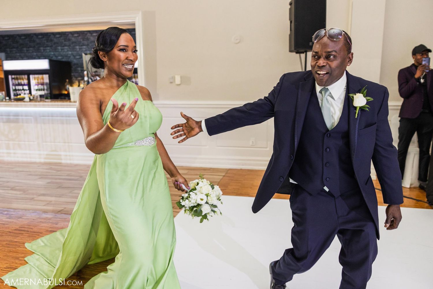 A couple shares a lively dance moment at their wedding, with the bridesmaid in mint green and groom in navy suit.