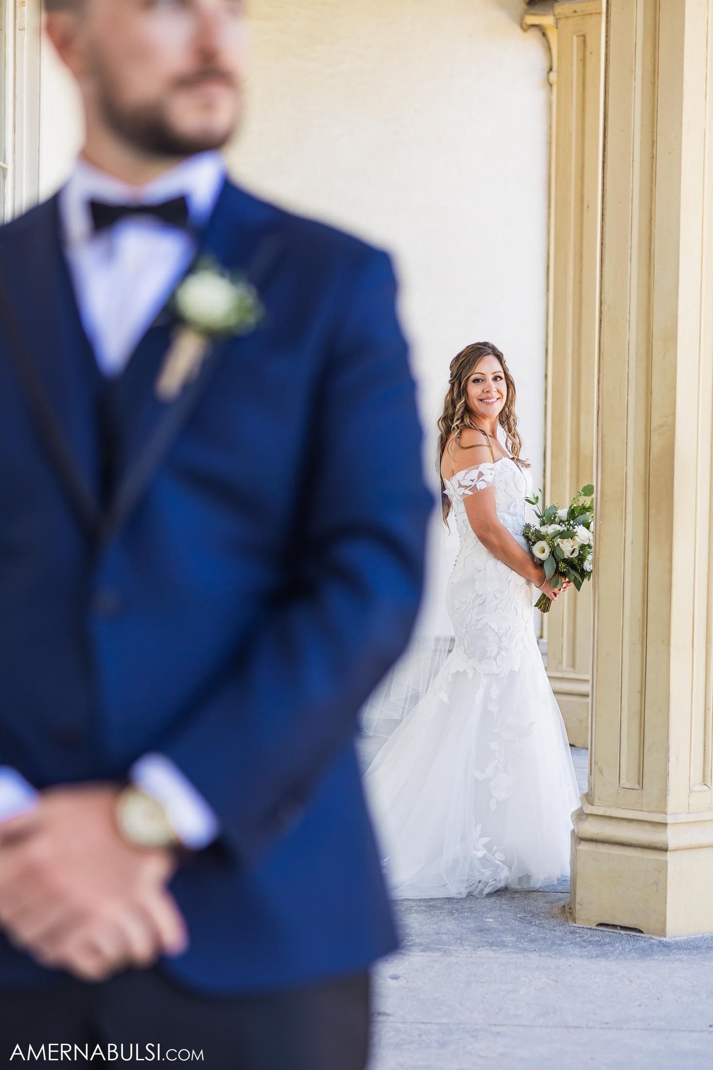 First look wedding photo with navy suit and white dress against classical architecture.