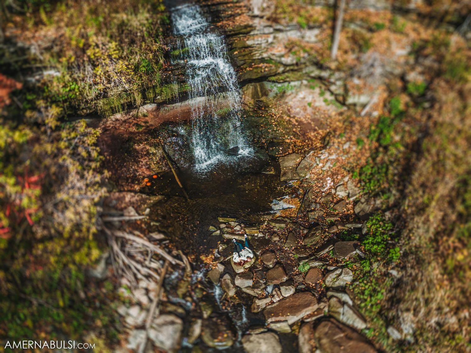 Small waterfall cascades down rocky cliff face surrounded by autumn colors.