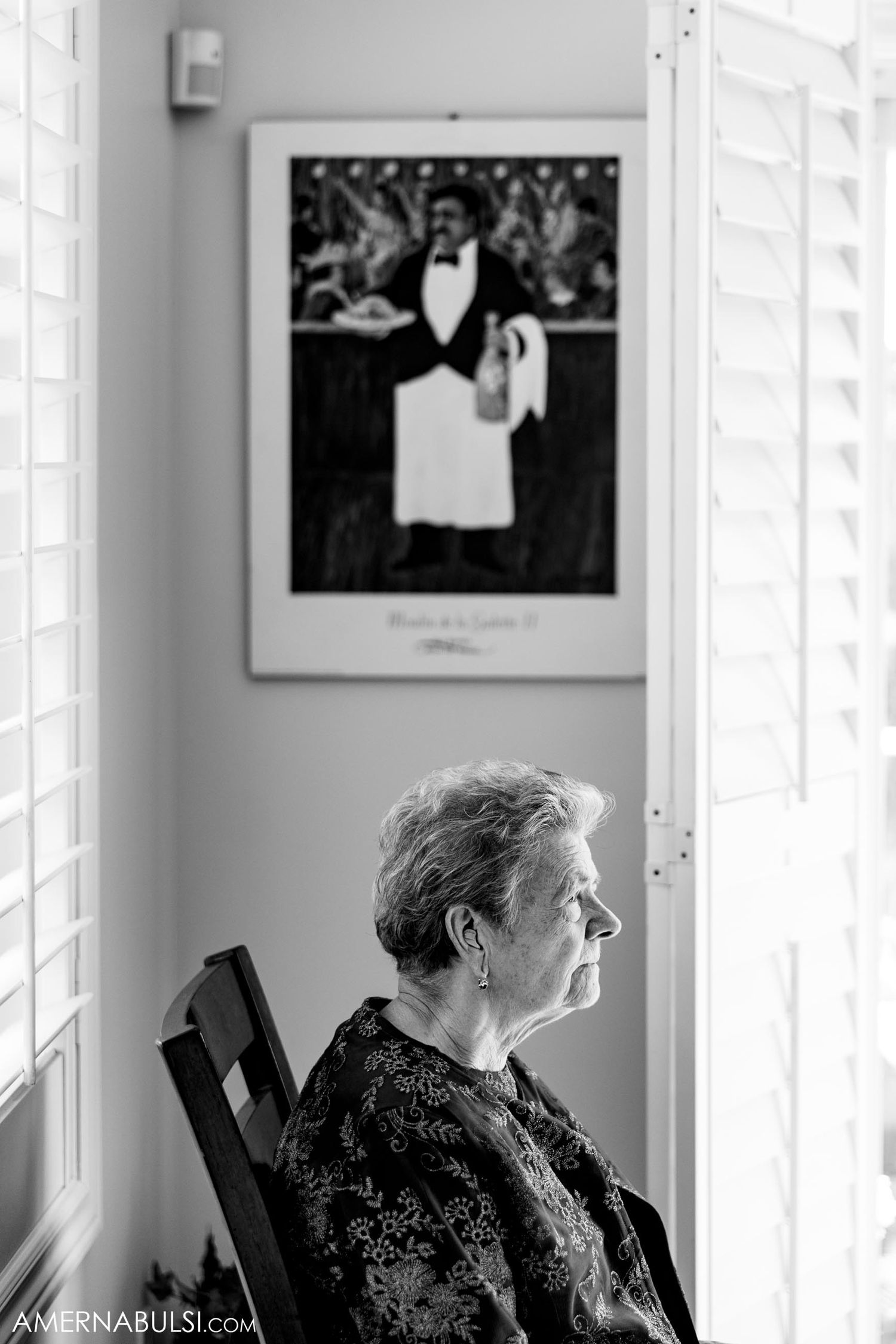 Artistic black and white portrait with vintage waiter photograph hanging on wall.