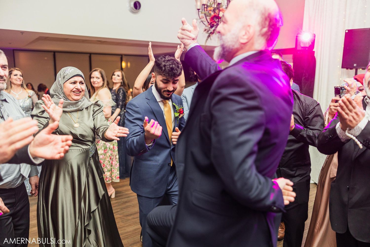 Party guests dancing and celebrating with enthusiasm at an indoor wedding reception.