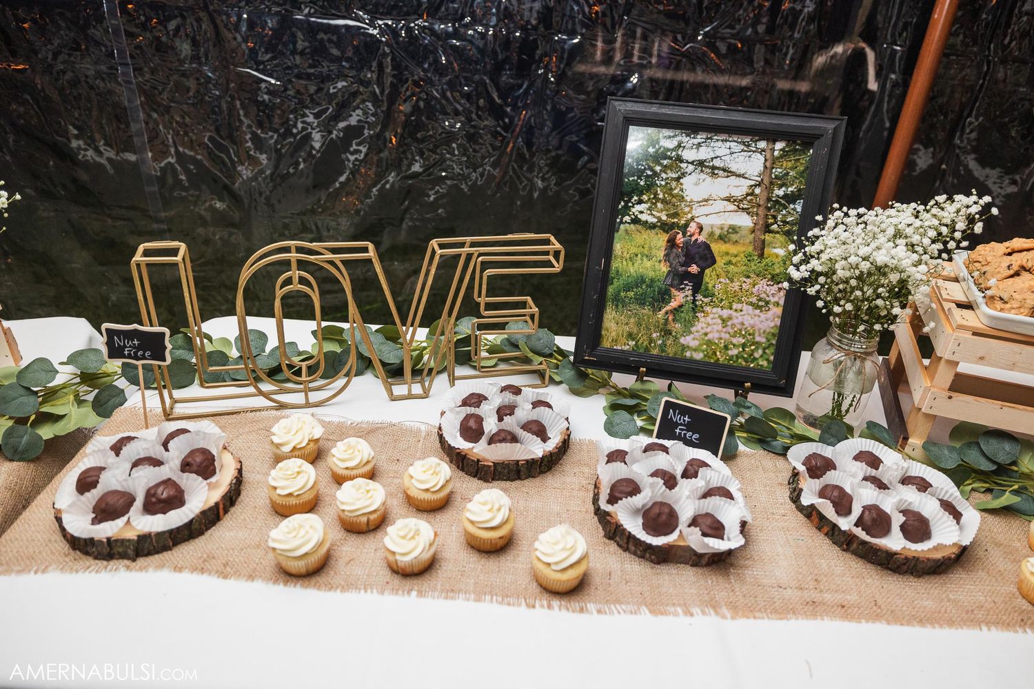 Rustic dessert table with LOVE sign, cupcakes, and framed photos at wedding reception.