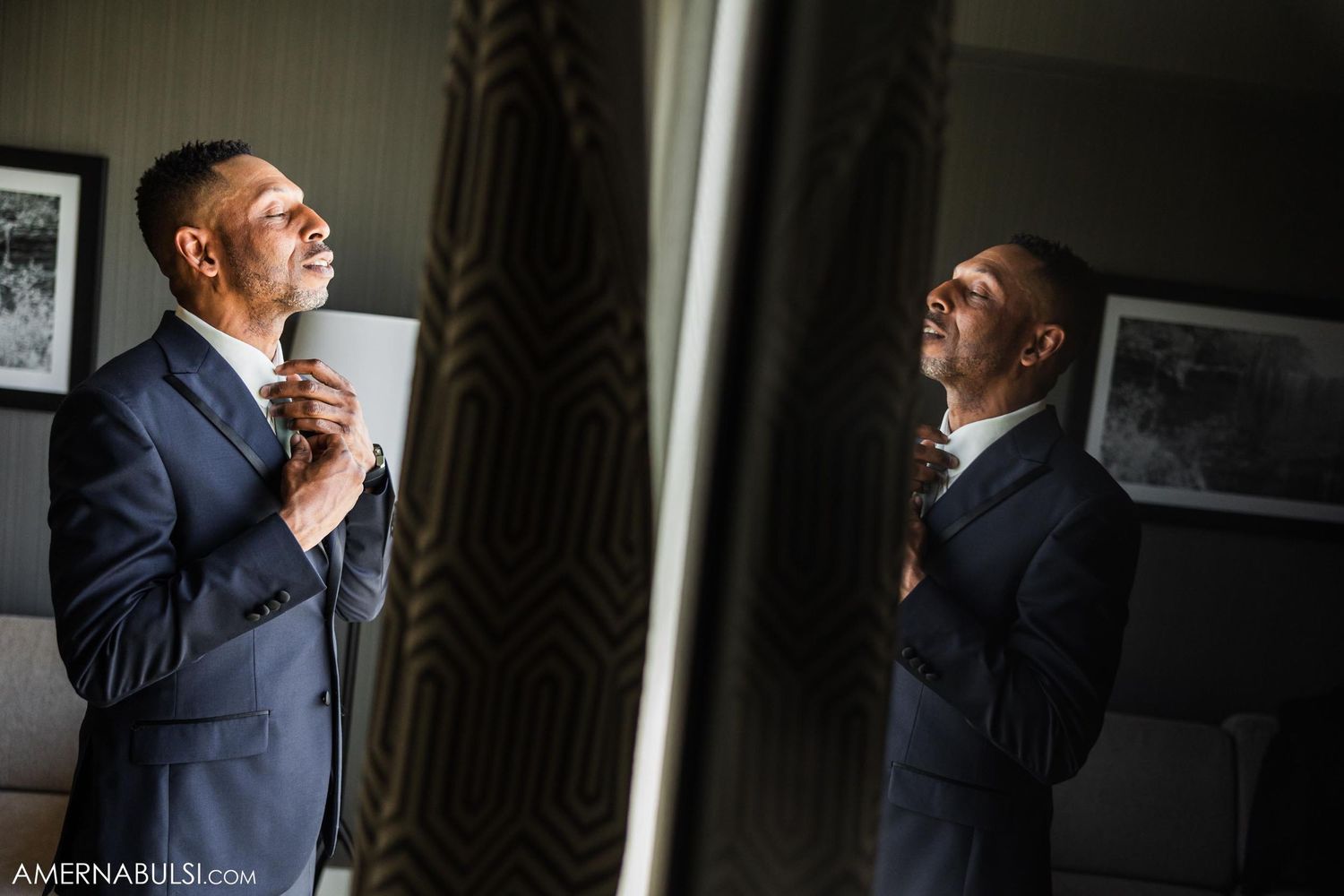 Groom adjusting his tie while looking in a mirror during wedding preparations.