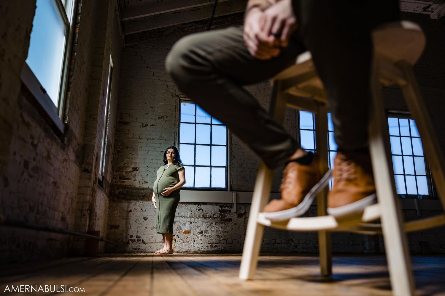Creative composition of maternity photoshoot in industrial space with large windows.