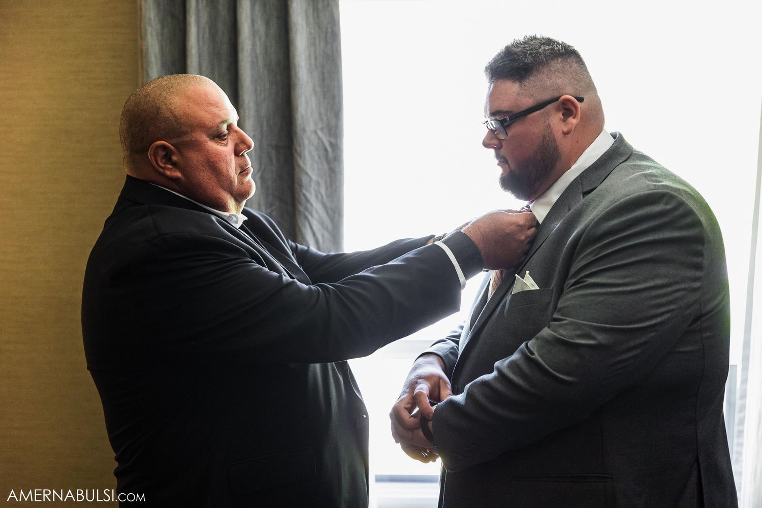 Man helping to adjust another man's tie in a formal setting.
