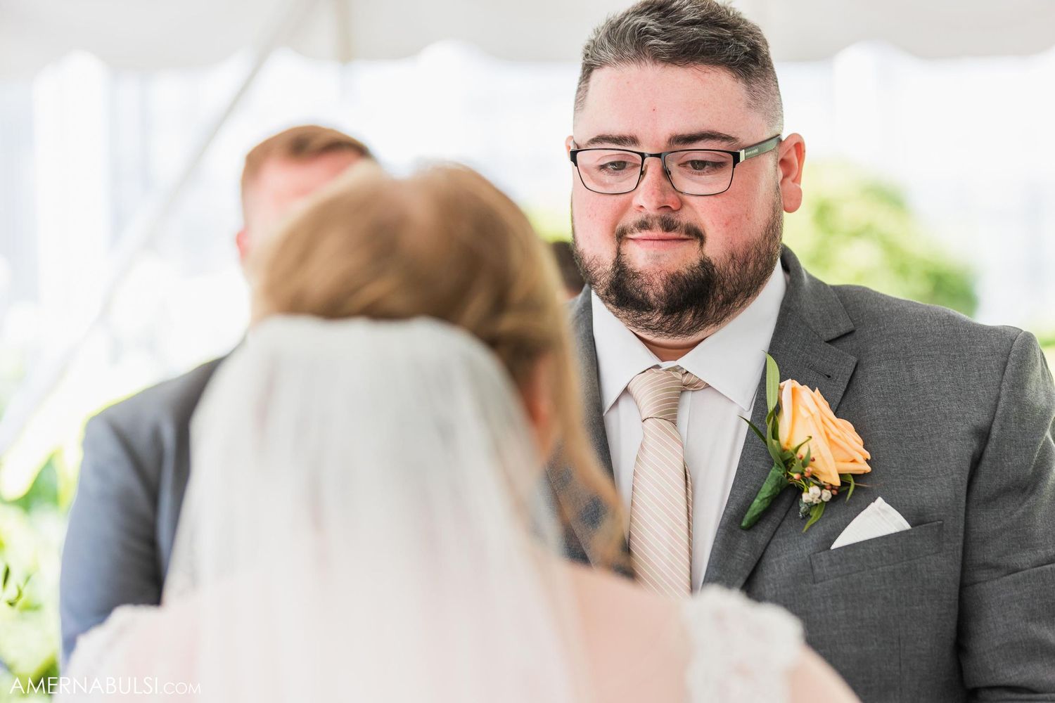 Groom with boutonniere smiling during outdoor wedding ceremony.