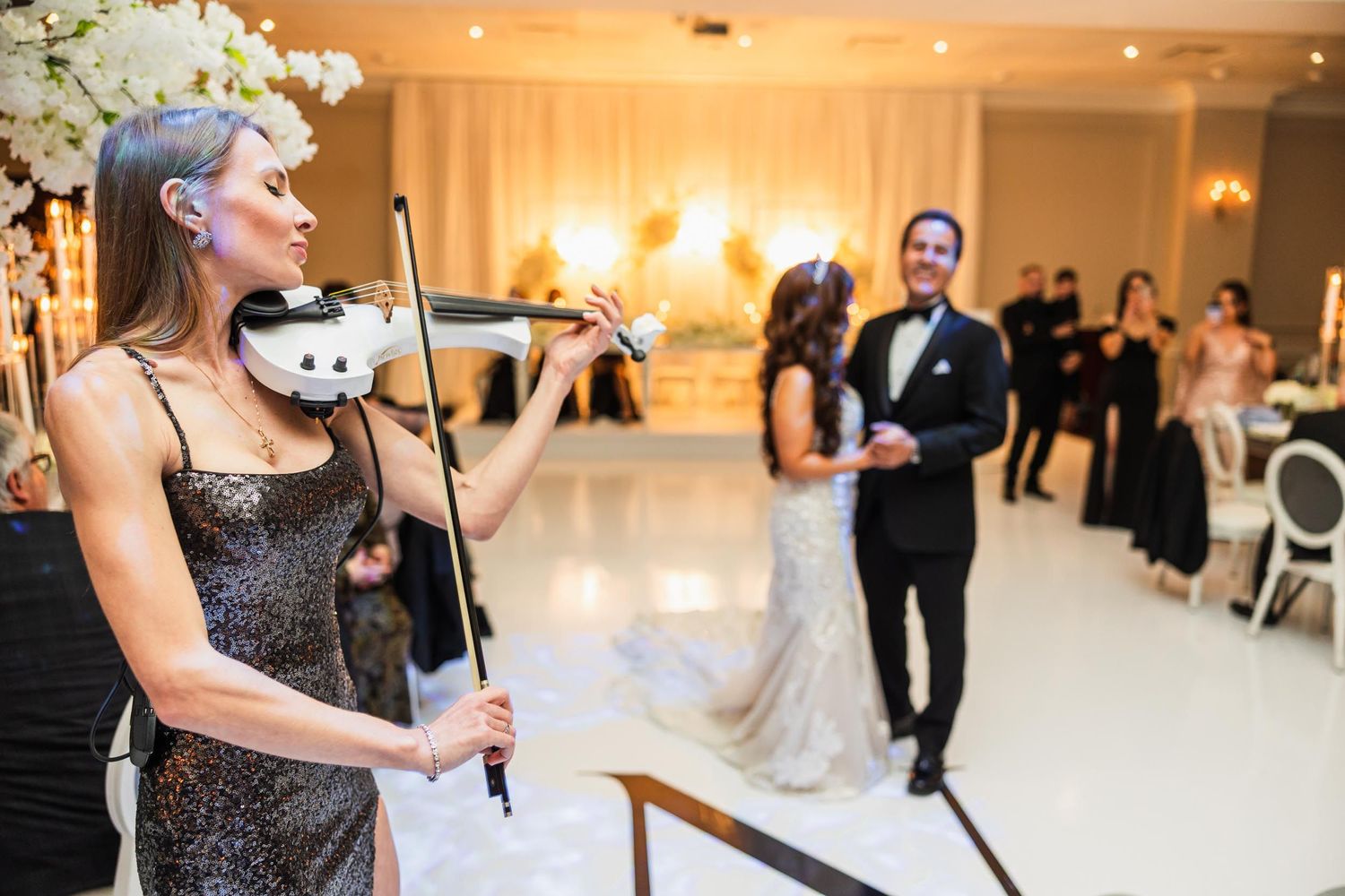 Violinist performs at elegant wedding reception in white decorated ballroom.