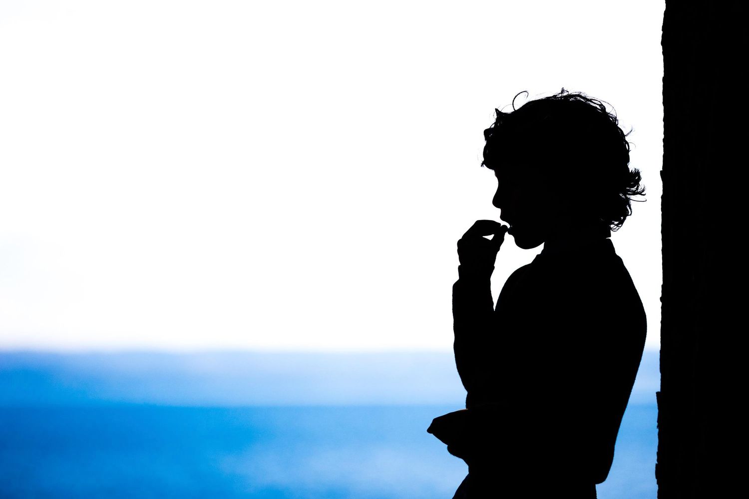 Silhouette profile of a figure against a blue ocean background.