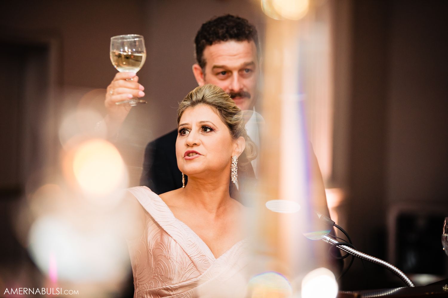 Wedding reception guests enjoying drinks and conversation in warm ambient lighting.