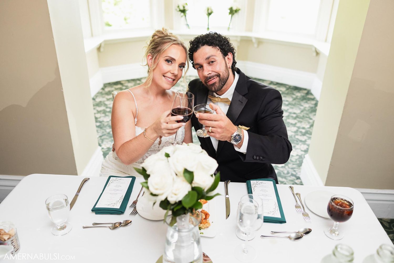 Couple looking at their phones while seated at an elegant white dining table with floral centerpiece.