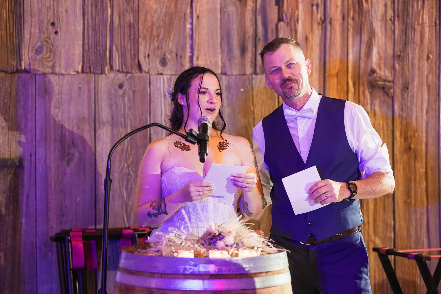 Wedding couple making announcements under purple lighting in rustic wooden venue.