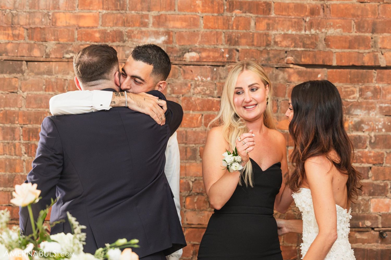 Wedding party members sharing emotional moments against a rustic brick wall backdrop.