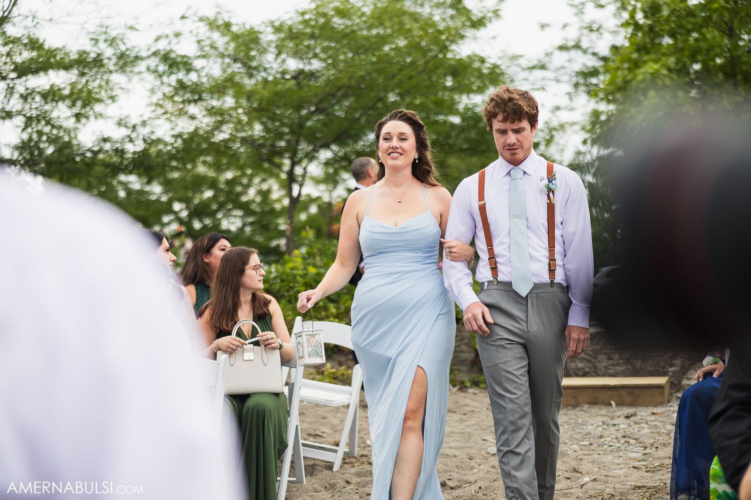 Wedding attendees in light blue dresses and gray suits gathering at an outdoor venue.