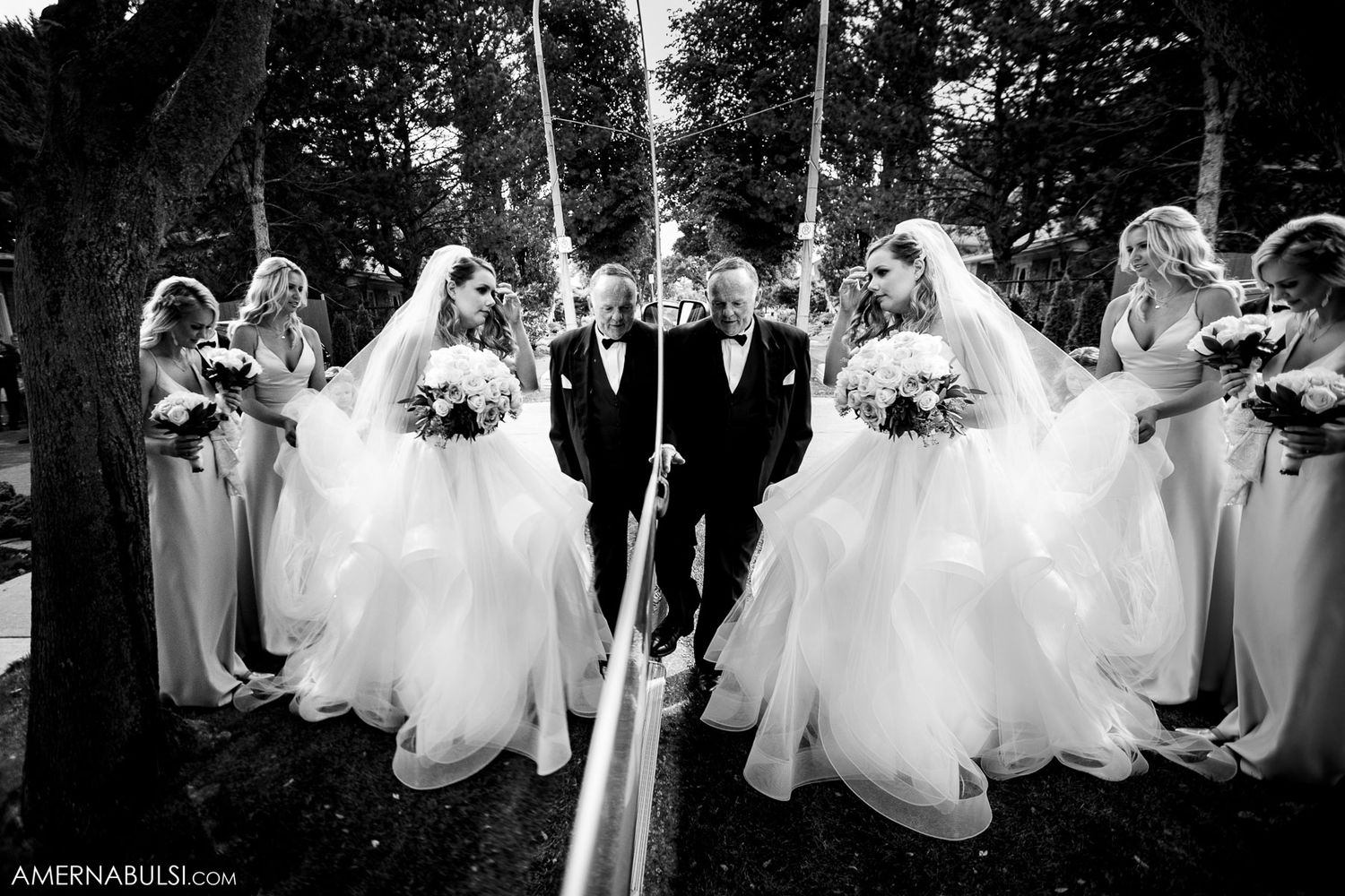 Row of young attendants in white dresses walking together outdoors in black and white photography.