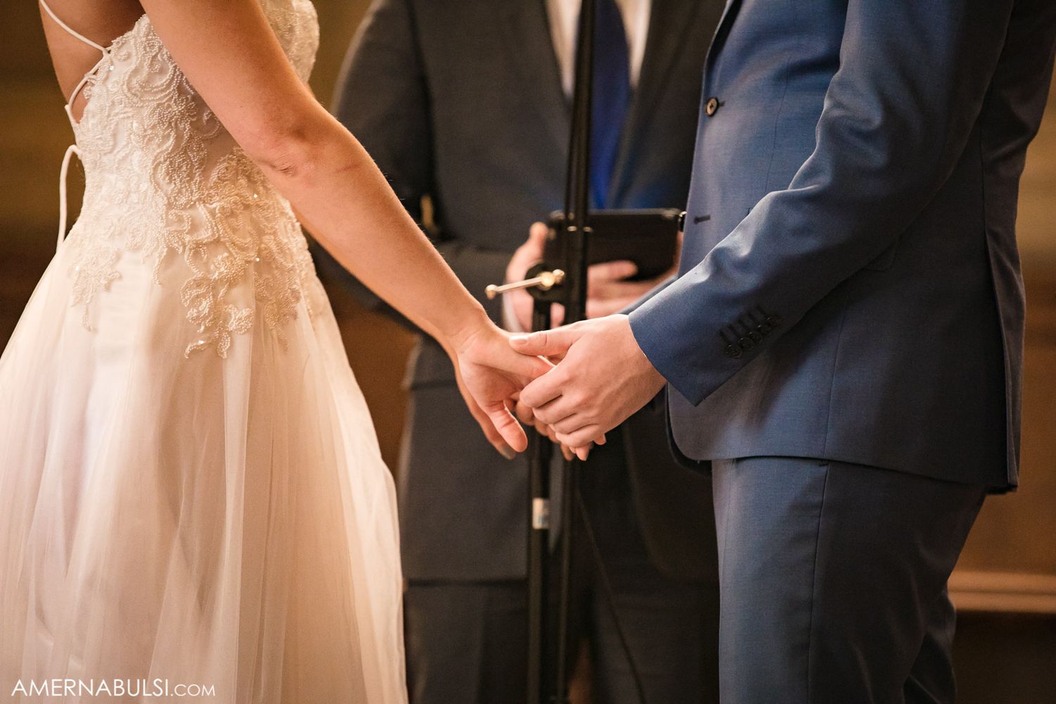 Close up of a couple holding hands during their wedding ceremony with officiant in background.