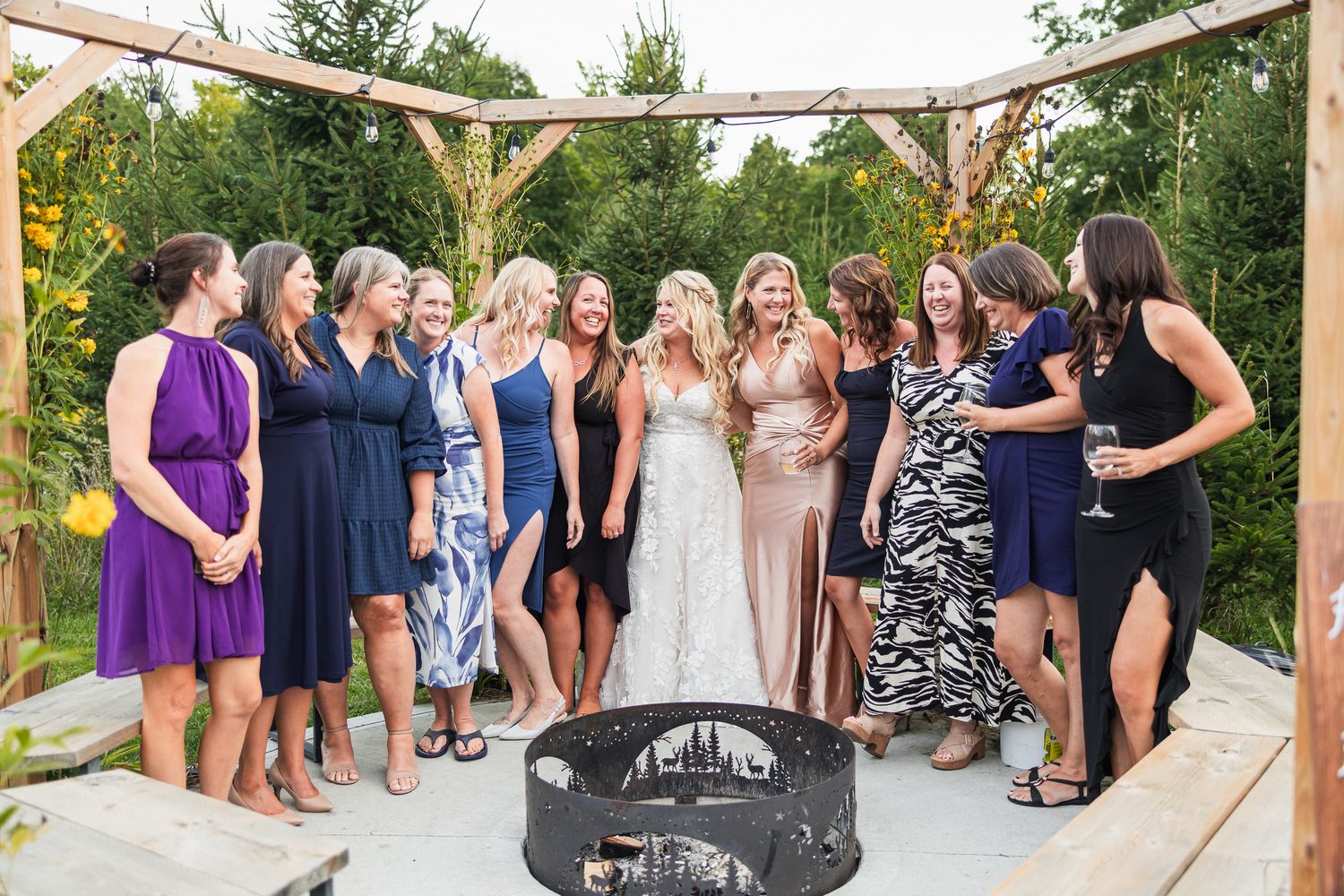 A group in formal attire poses together on an outdoor wooden deck under a rustic wooden arbor.