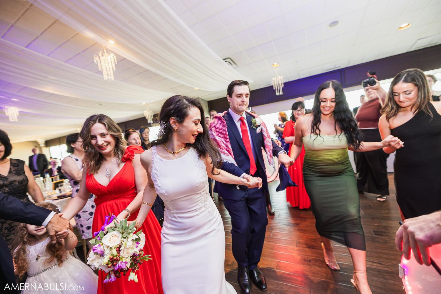 Wedding party procession on dance floor with guests in red and formal attire.