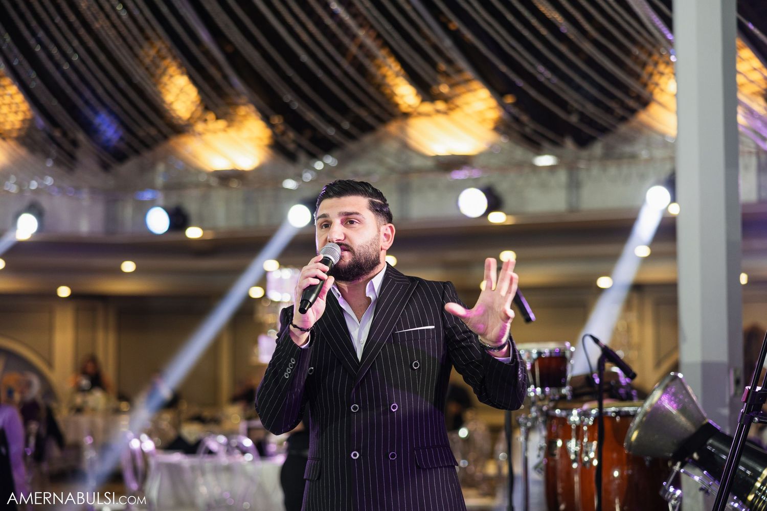 A performer in a pinstriped suit sings passionately on stage at an elegant wedding reception.