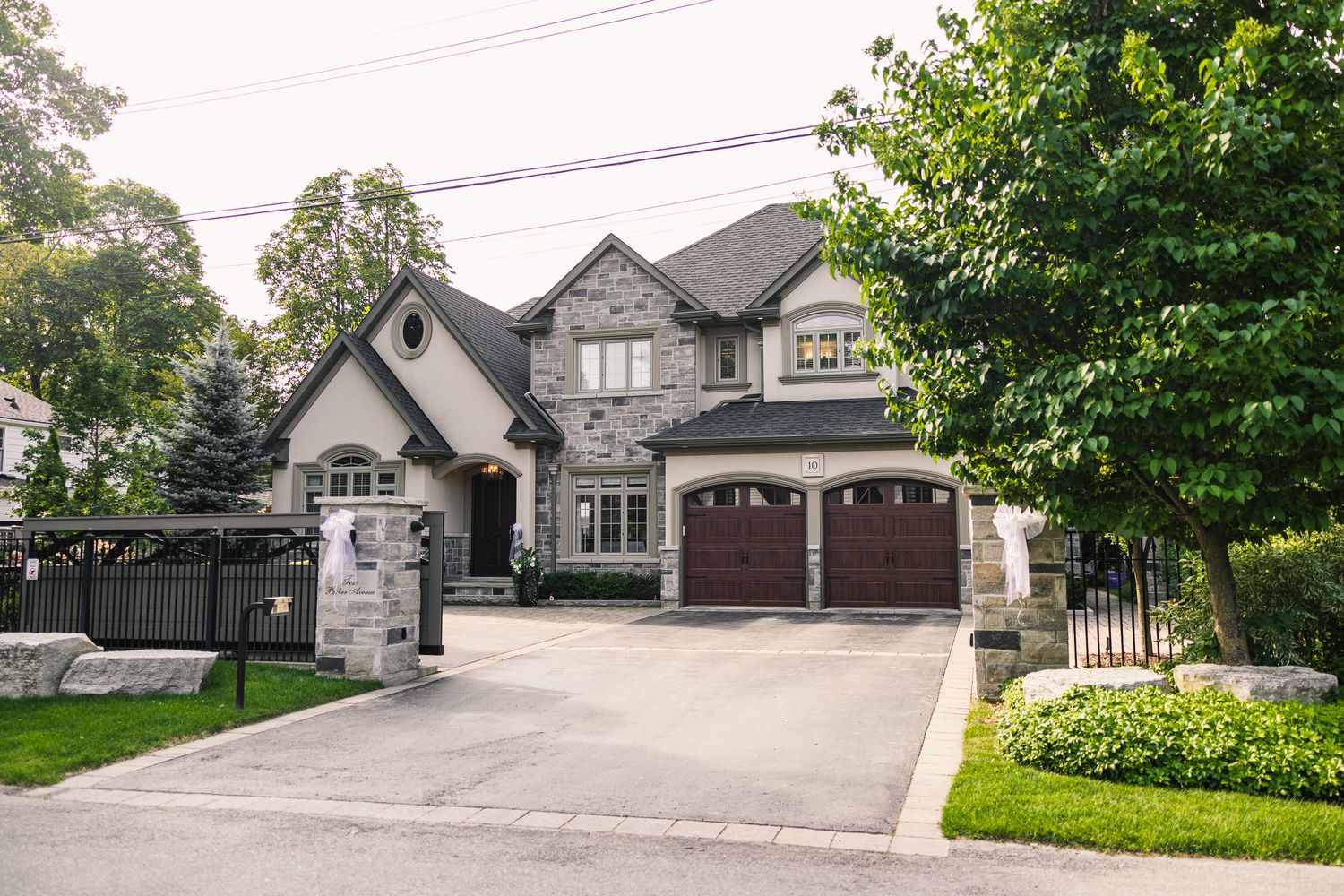 Elegant stone and brick two-story home with double garage, manicured lawn, and lush trees in a suburban neighborhood.