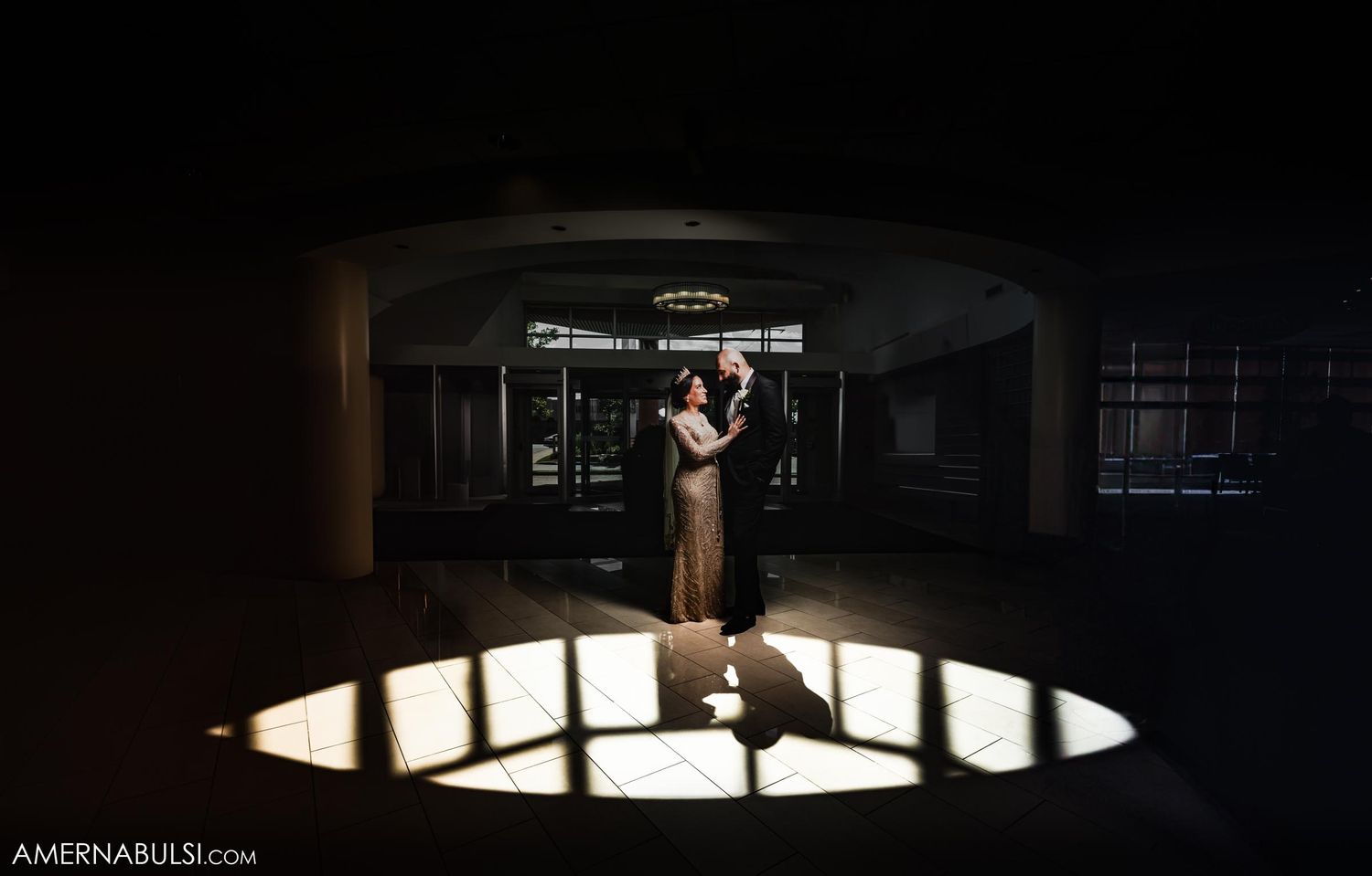 Dramatic silhouette of wedding couple dancing in spotlight on dark stage.