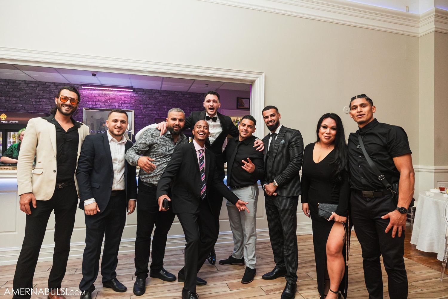 Group photo of wedding party members in formal attire posing together at reception.