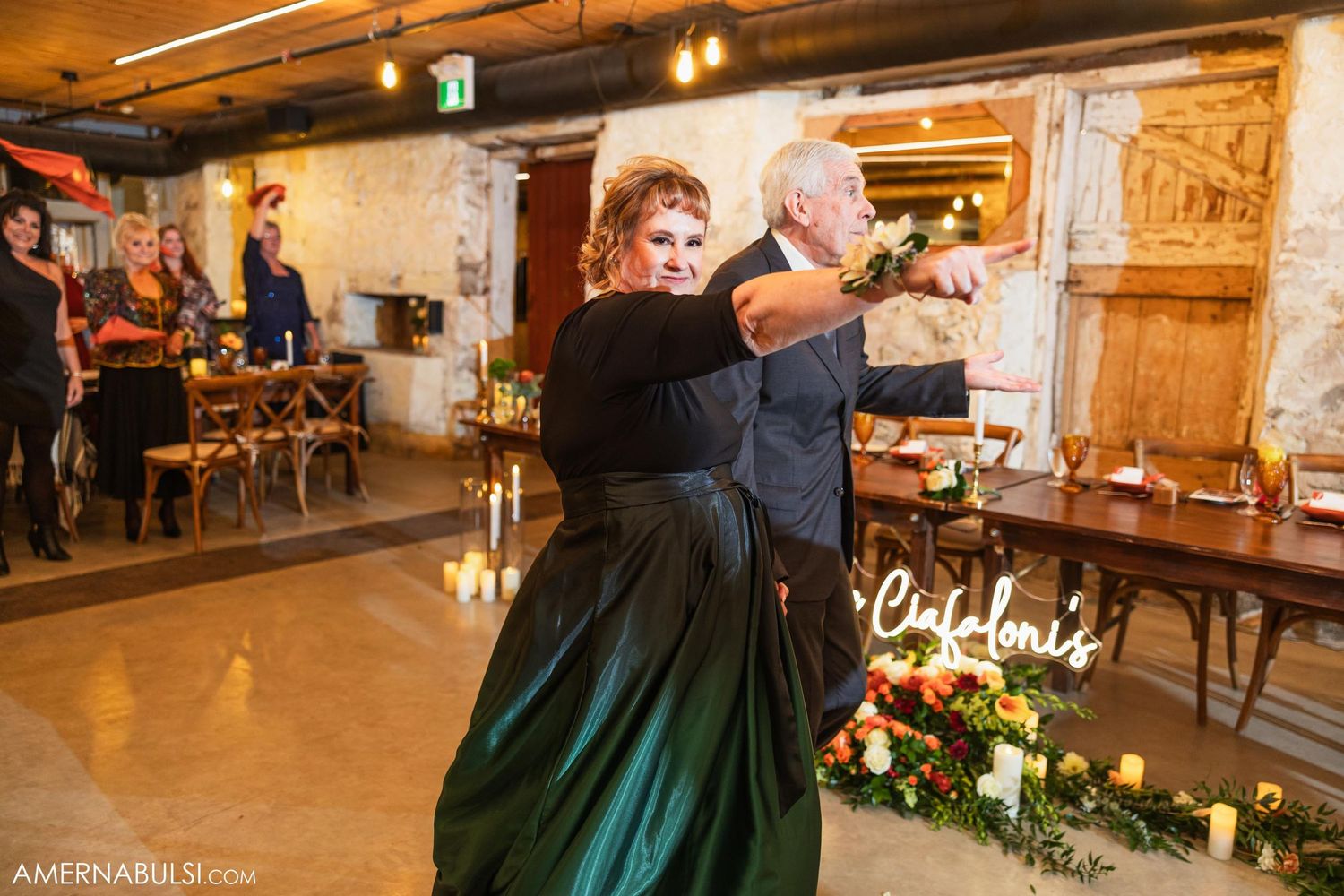 Wedding guests sharing a dance moment at rustic reception venue with wooden floors.