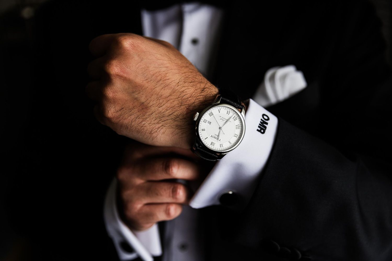 Close-up of a wrist watch on a formal suit sleeve with white cuff visible.