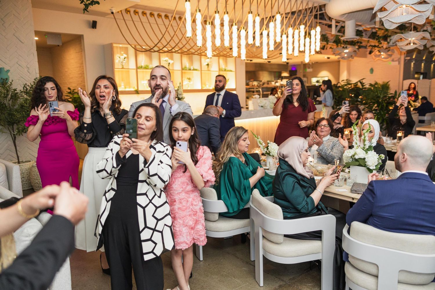 Wedding guests gather at an elegant reception venue with hanging pendant lights and modern decor.