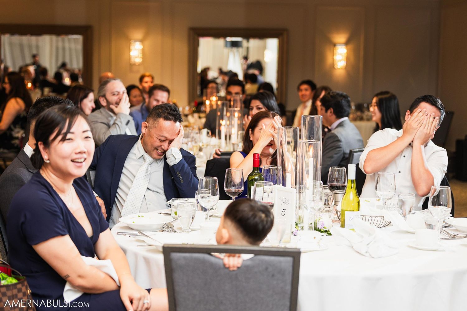 Wedding guests laugh and react during reception dinner at elegantly decorated tables.