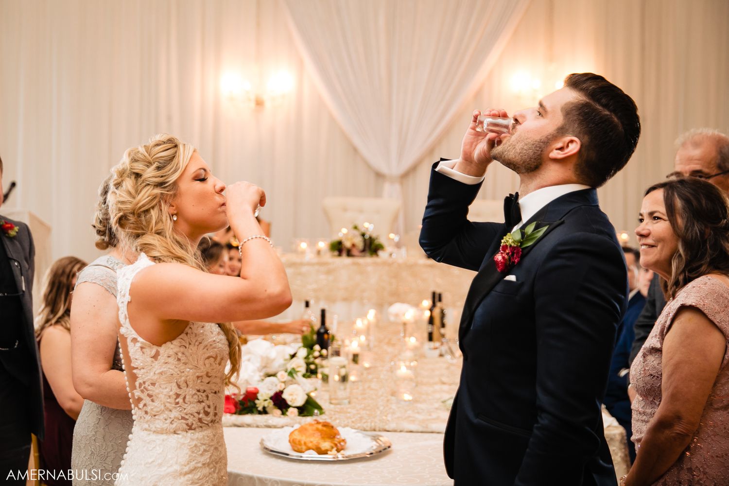 Wedding guests at an elegant reception raise their glasses in a celebratory toast at a beautifully decorated venue.