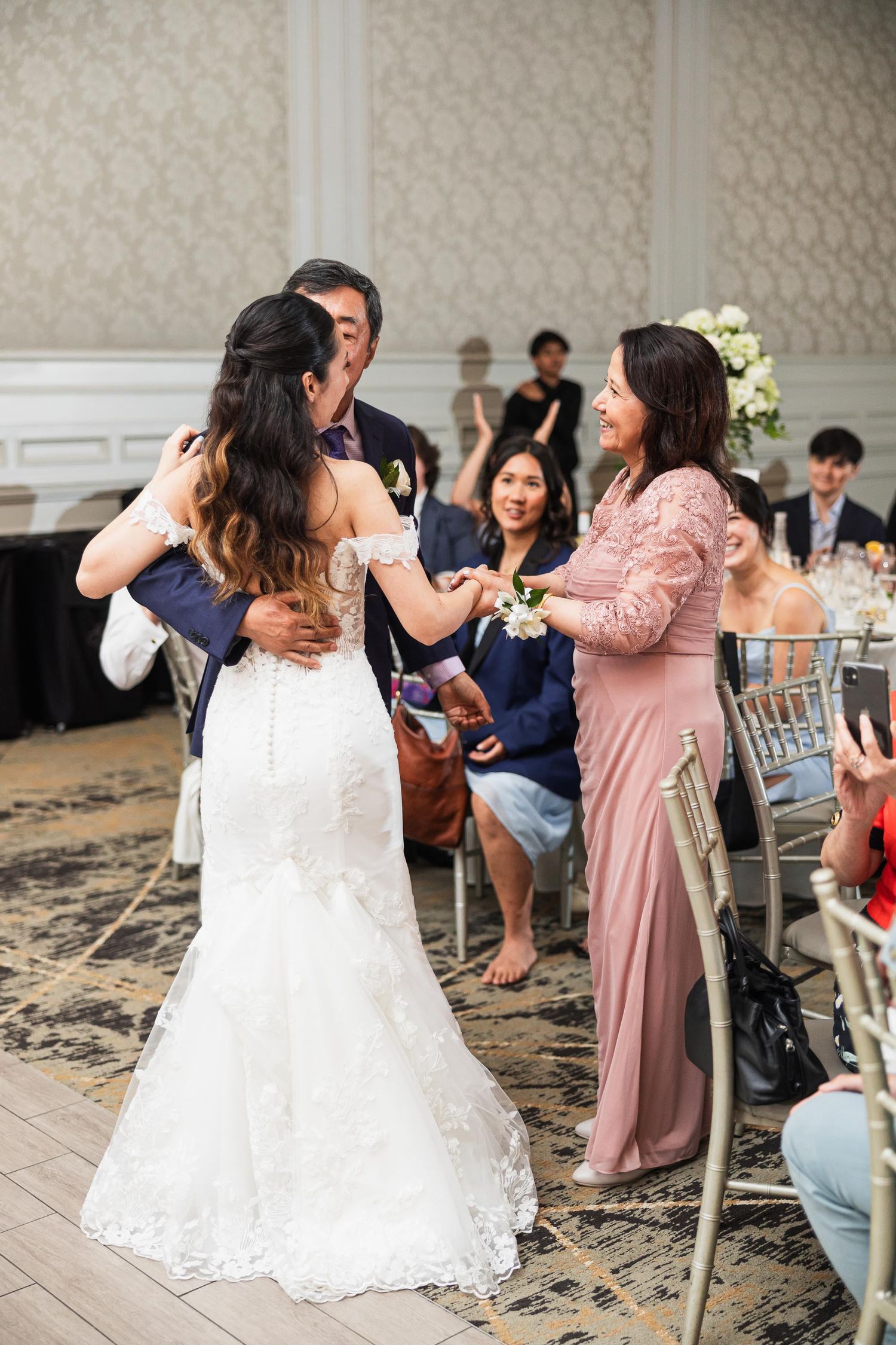 A bride in a lace wedding gown dances with guests during a reception celebration.