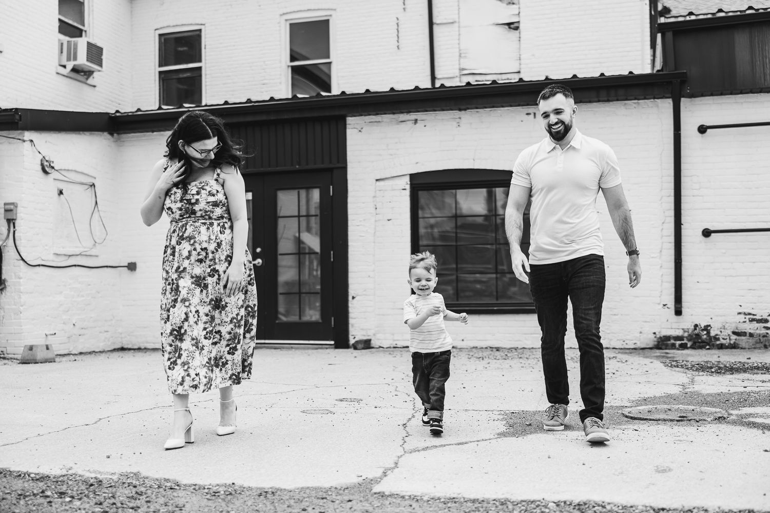 Family walking together outdoors against white building in black and white photograph.