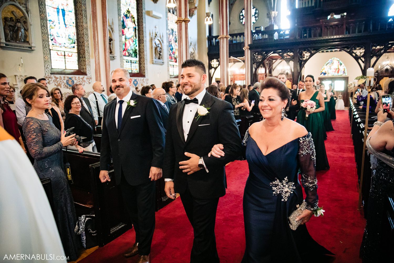 Wedding ceremony guests gathered inside a grand church with red carpeting and ornate decor.