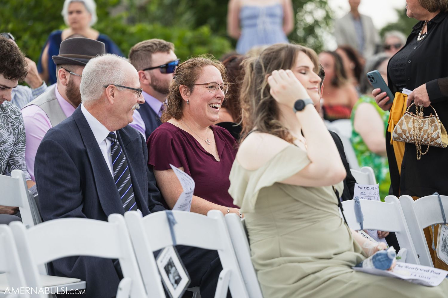 Wedding reception guests mingle and celebrate at outdoor tables with white chairs.