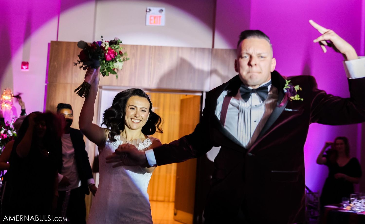 Celebration in wedding reception venue with dramatic pink lighting and raised hands.