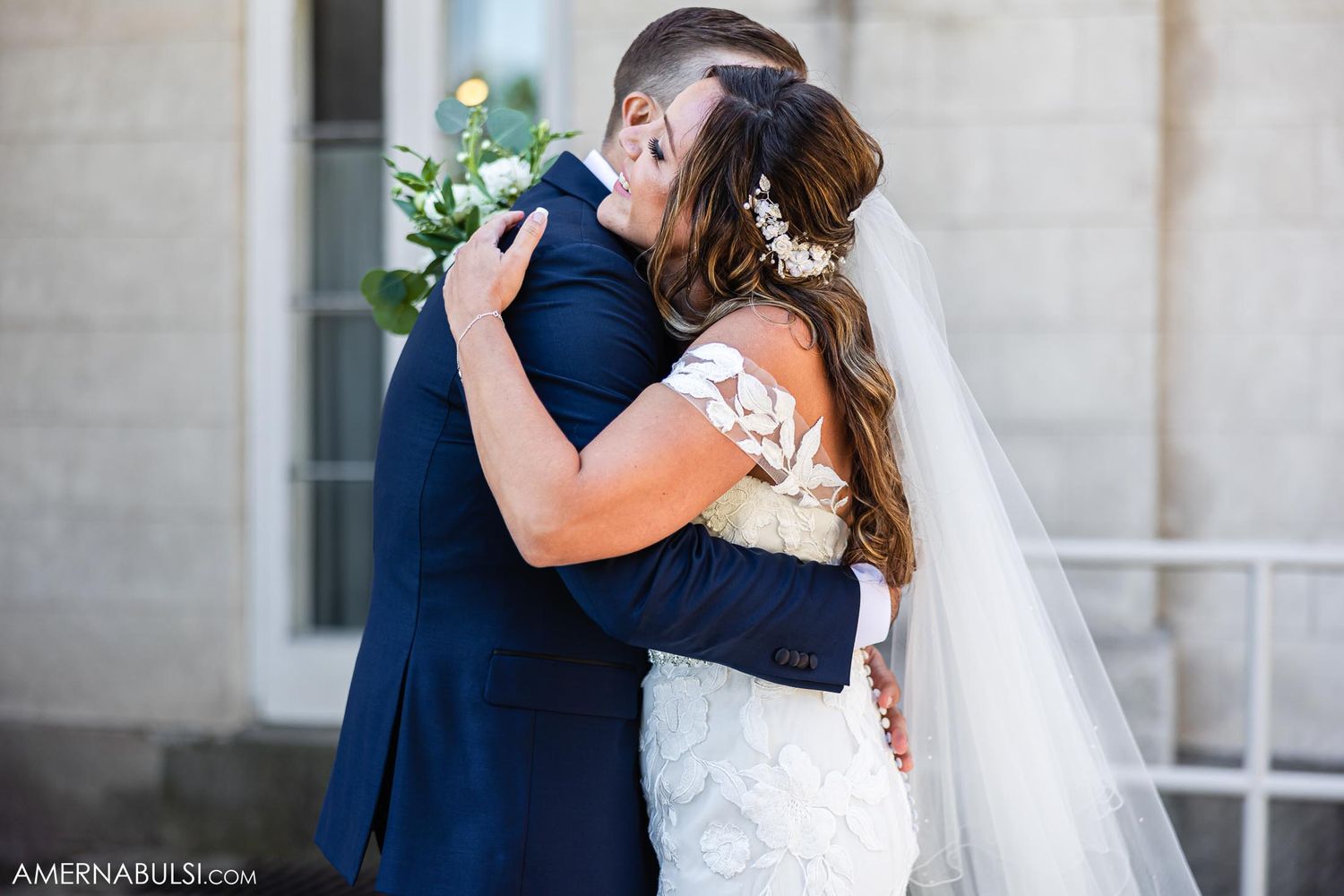 Romantic wedding embrace between couple in navy suit and lace gown.