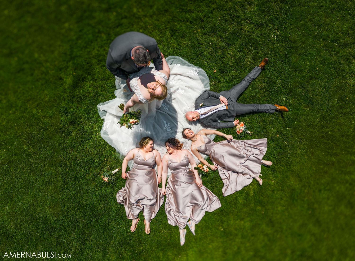 Aerial view of wedding party lying in a circle formation on green grass.
