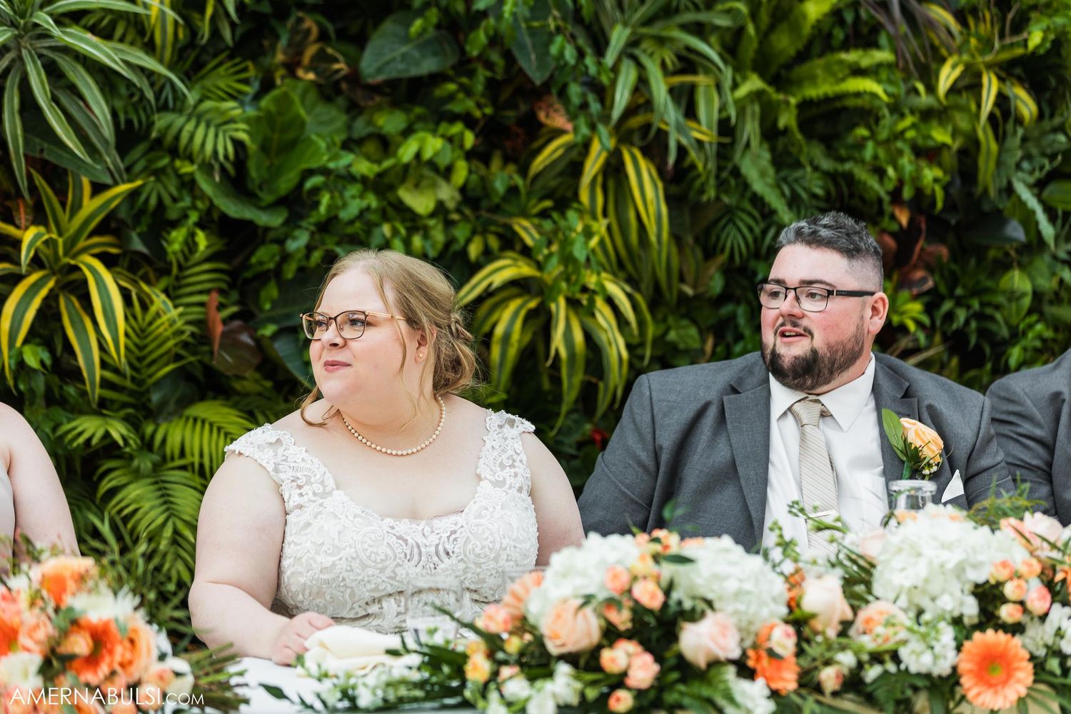 A couple sits at an elegant wedding reception table decorated with lush floral arrangements.