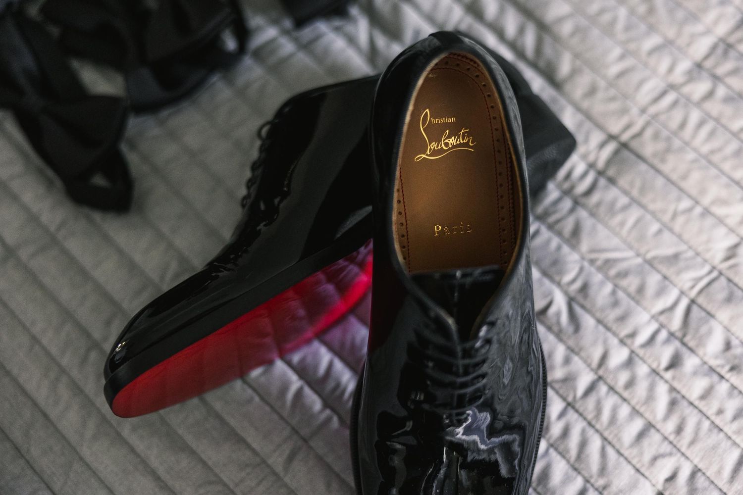 Close-up of black patent leather Christian Louboutin dress shoes with signature red sole.
