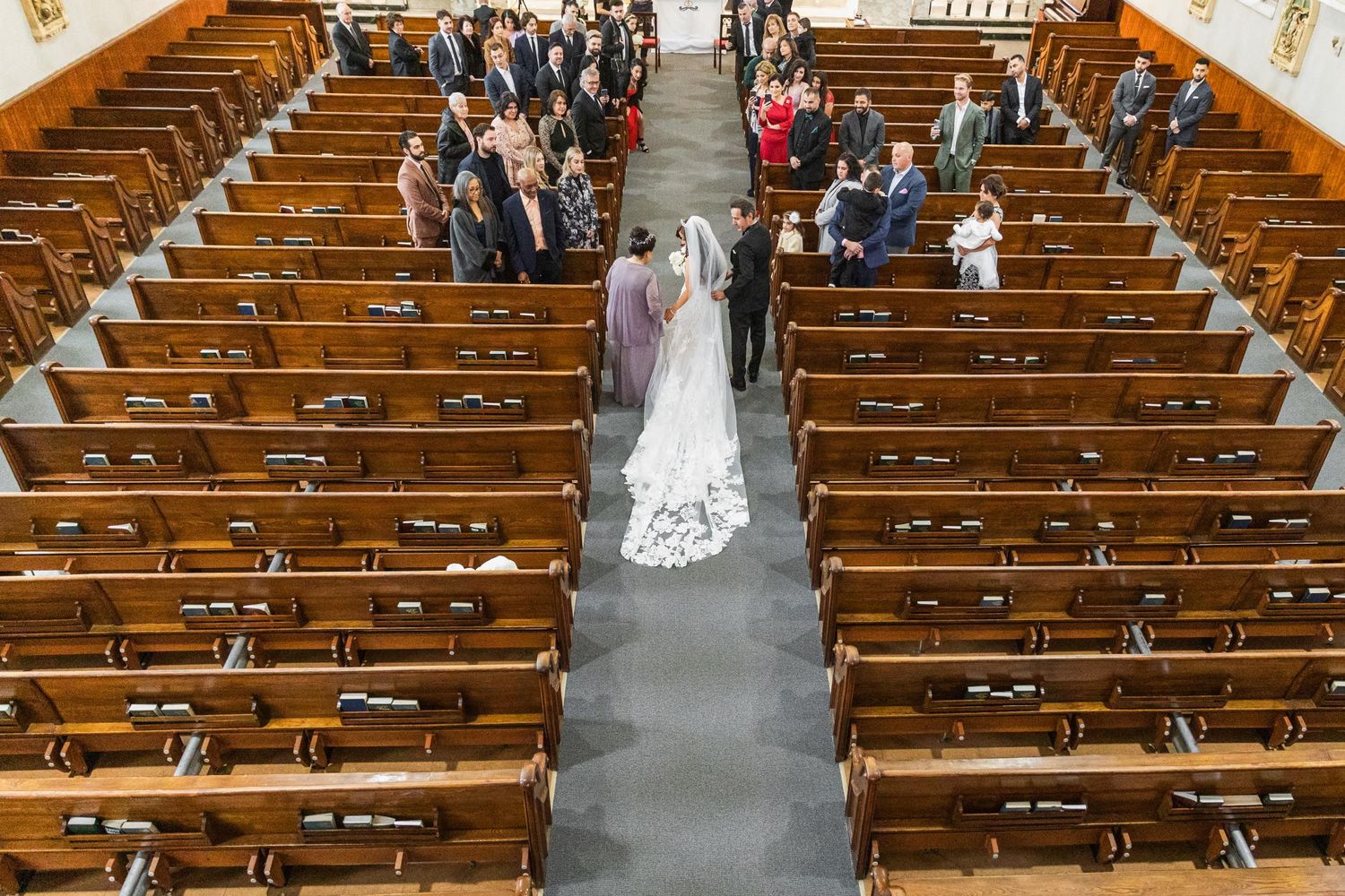 An aerial view of newlyweds walking down the church aisle surrounded by wooden pews filled with guests.
