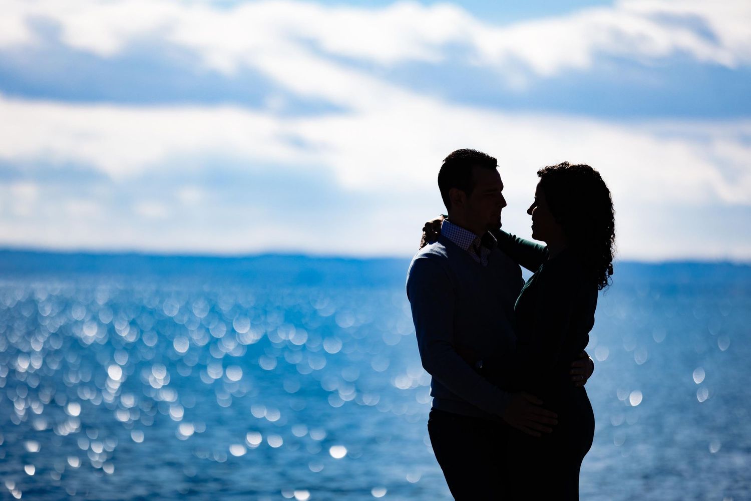 Silhouette of a couple embracing against a scenic water view with mountains in the background.