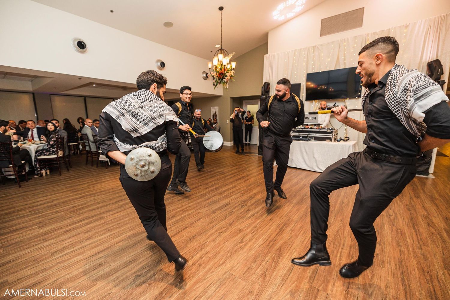 Groomsmen perform an energetic dance routine on a wooden floor at a wedding reception.
