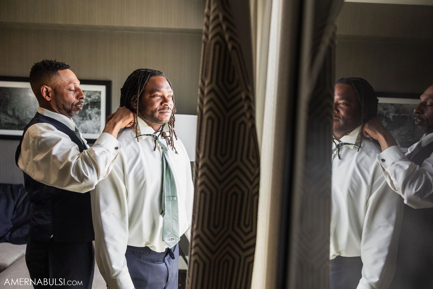Wedding groomsmen helping each other with final touches in a dressing room.