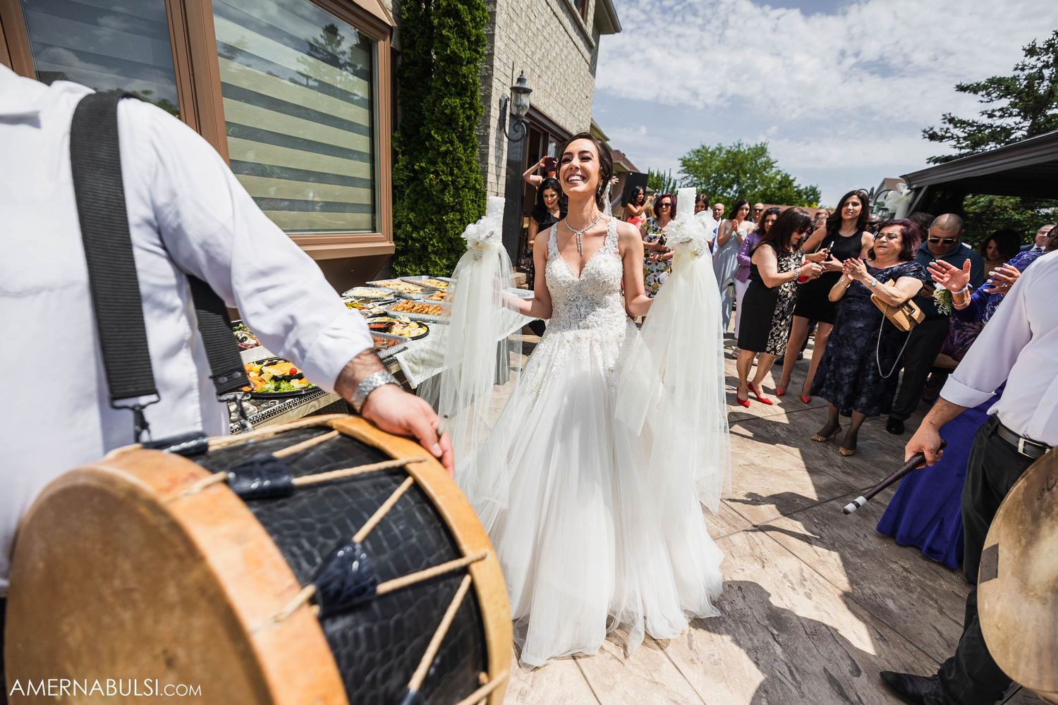 Outdoor wedding celebration with musicians playing drums while guests dance on a sunny patio.