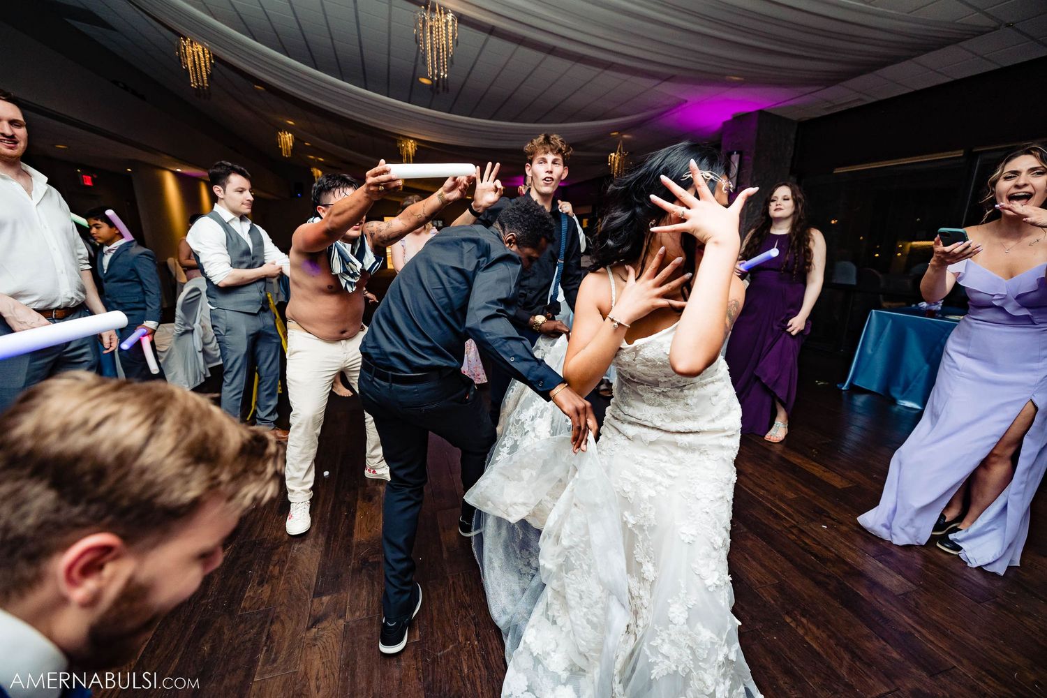 Energetic dance party at wedding reception with guests dancing under purple lighting.