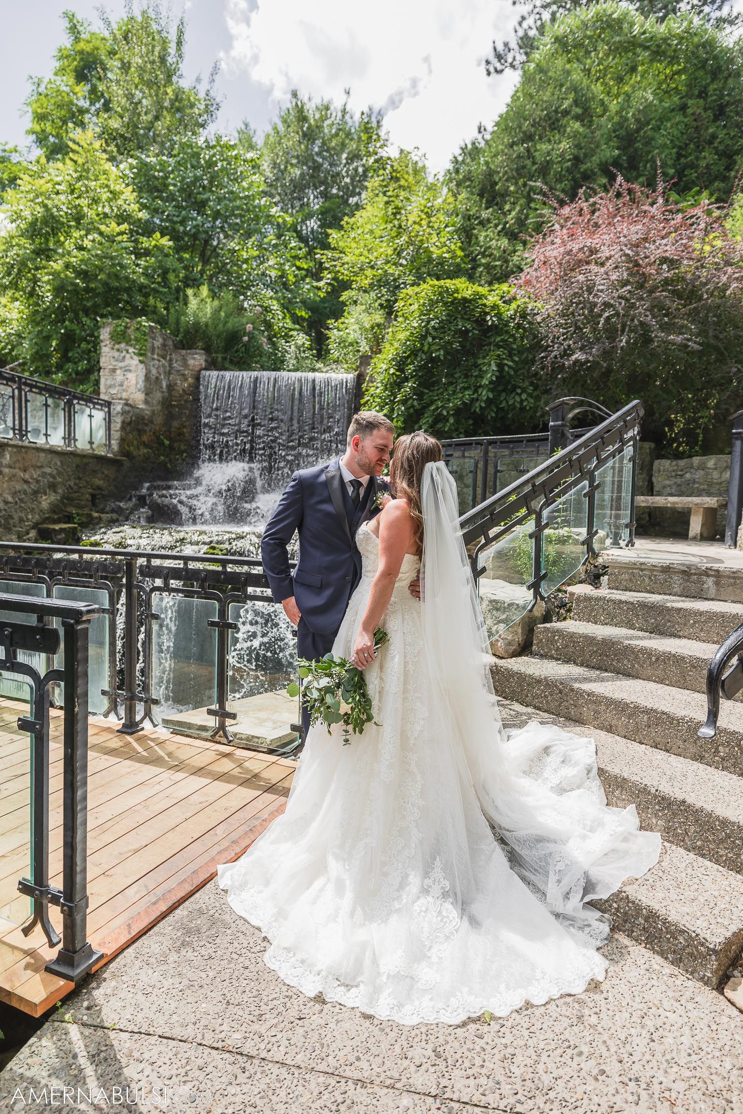 Couple poses by cascading waterfall on stone staircase during wedding photoshoot.