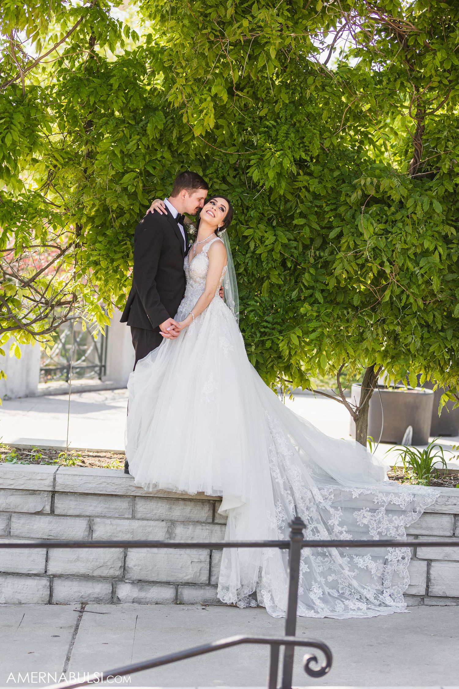 A beautiful wedding portrait taken on stone steps surrounded by green leaves and natural light.