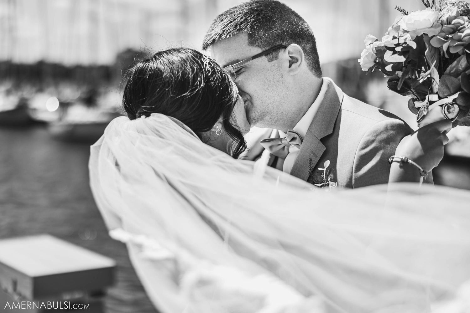 Black and white romantic wedding moment captured at a marina with flowing veil.