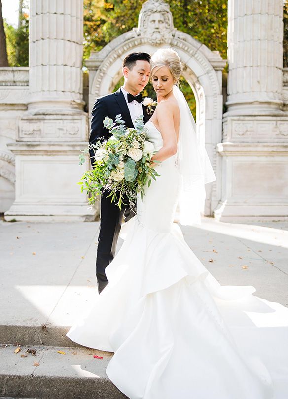 Elegant bride's dress flows dramatically against classical stone columns.