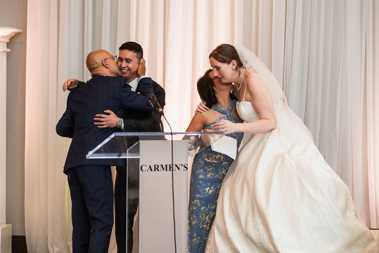 Wedding guests embracing near Carmen's podium during reception.